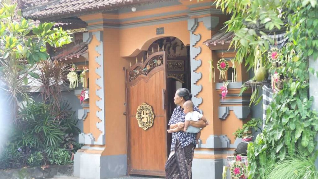 Seorang nenek Bali mengasuh cucunya sambil tetap mengenakan busana adat, mencerminkan keseharian yang sarat tradisi.