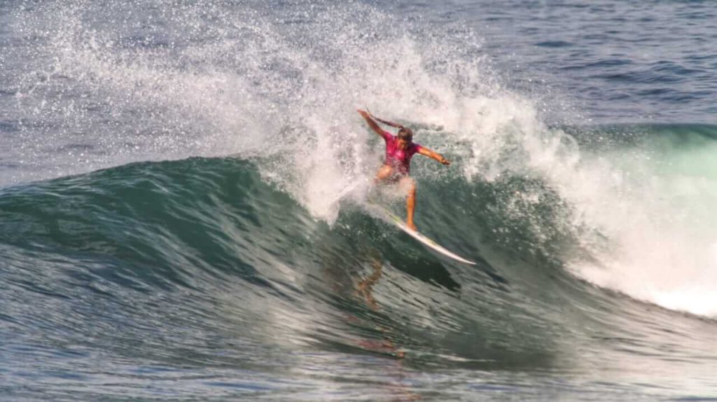Seorang peselancar berdiri di atas papan selancar, bersiap menghadapi ombak di laut.