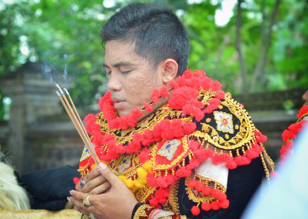 Penari topeng duduk hening sambil memegang sangkep dan dupa yang mengepul lembut.