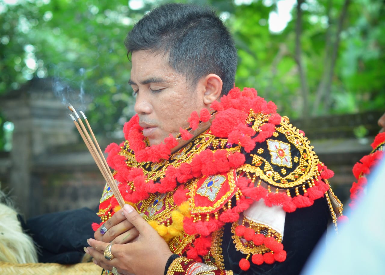 Penari topeng duduk hening sambil memegang sangkep dan dupa yang mengepul lembut.