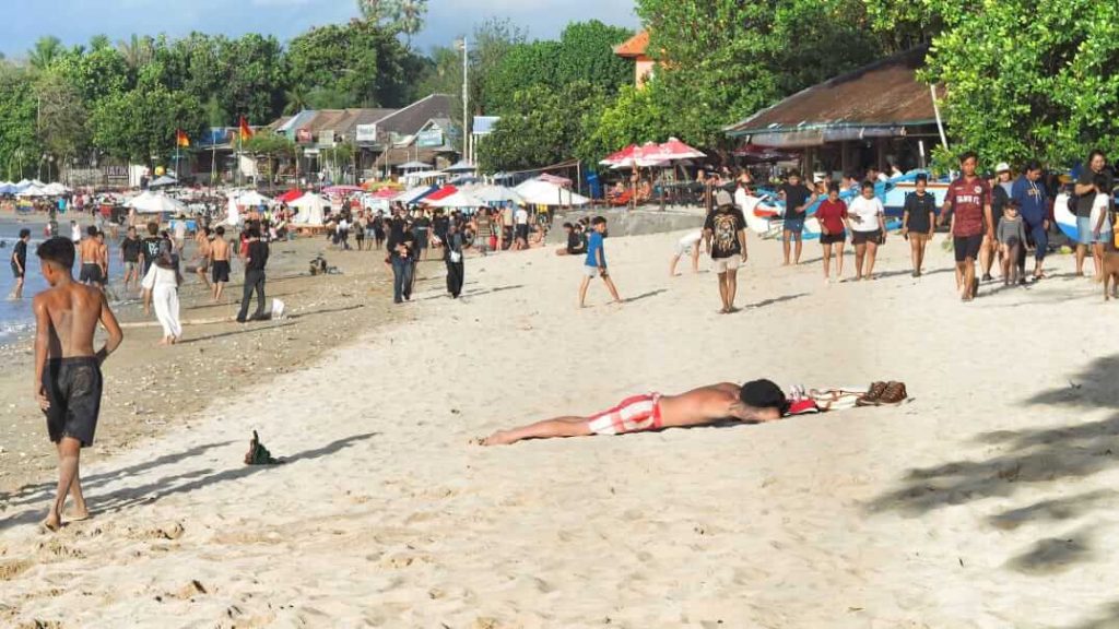 Turis asing berjemur di Pantai Muaya, Jimbaran, di tengah aktivitas masyarakat lokal.