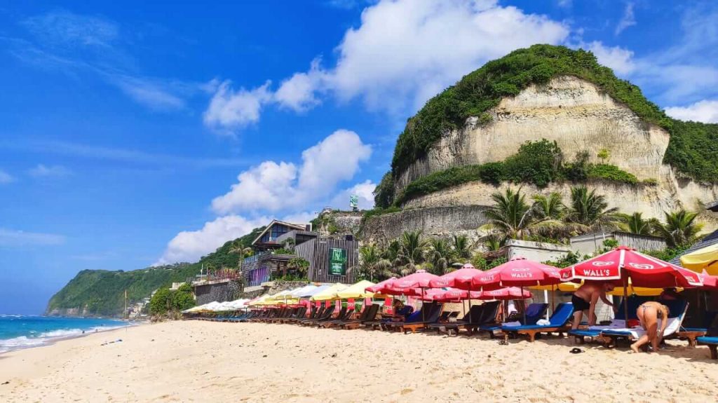 Wisatawan bersantai di long chair berpayung sambil menikmati Pantai Melasti Bali.