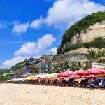 Wisatawan bersantai di long chair berpayung sambil menikmati Pantai Melasti Bali.