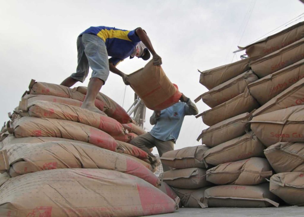 Para pekerja mengangkat karung semen bersama sebagai simbol nilai gotong royong dan kerja sama.