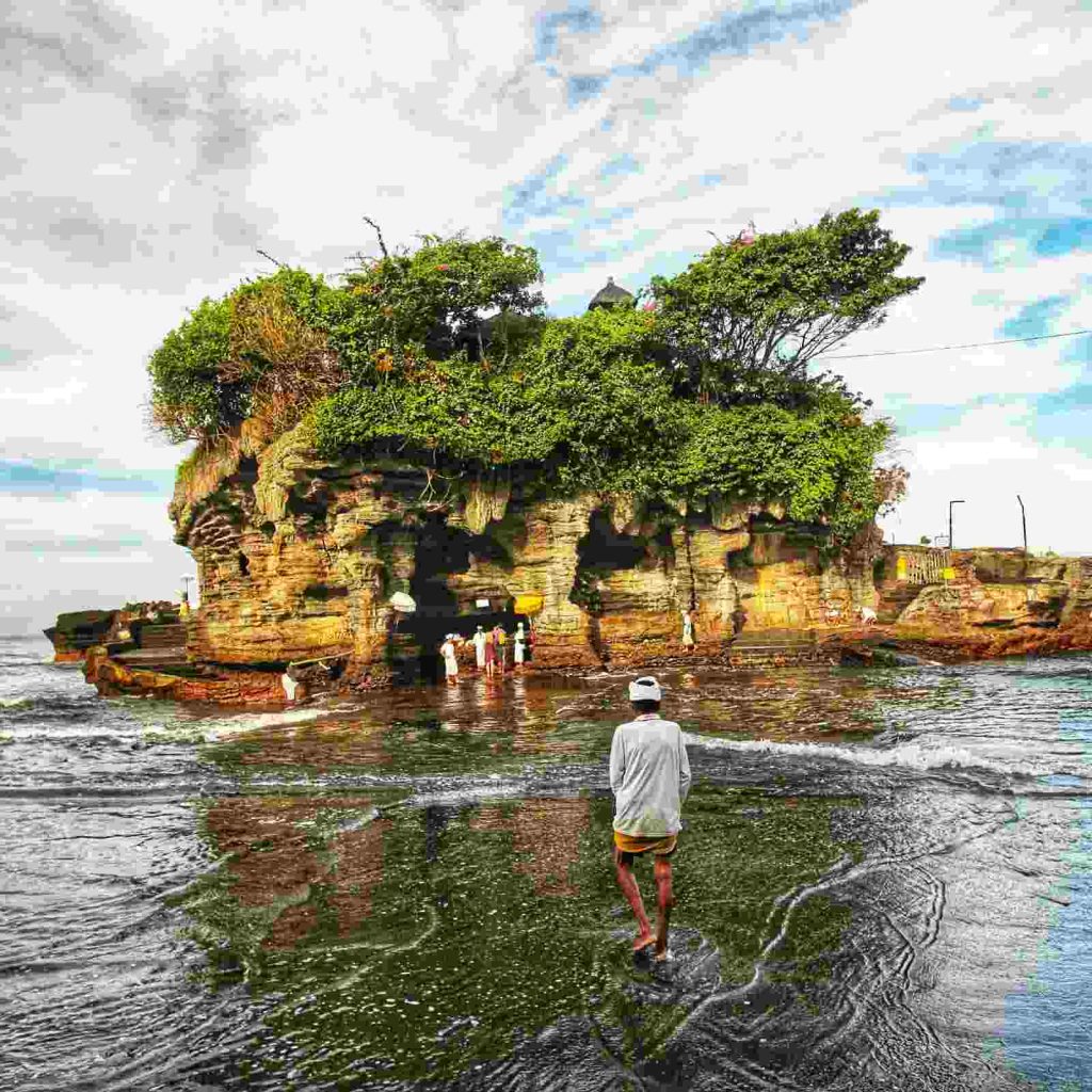 Pura Tanah Lot di tepi laut dengan ombak menghempas bebatuan, menjadi simbol budaya dan spiritualitas Bali.