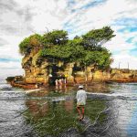 Pura Tanah Lot di tepi laut dengan ombak menghempas bebatuan, menjadi simbol budaya dan spiritualitas Bali.