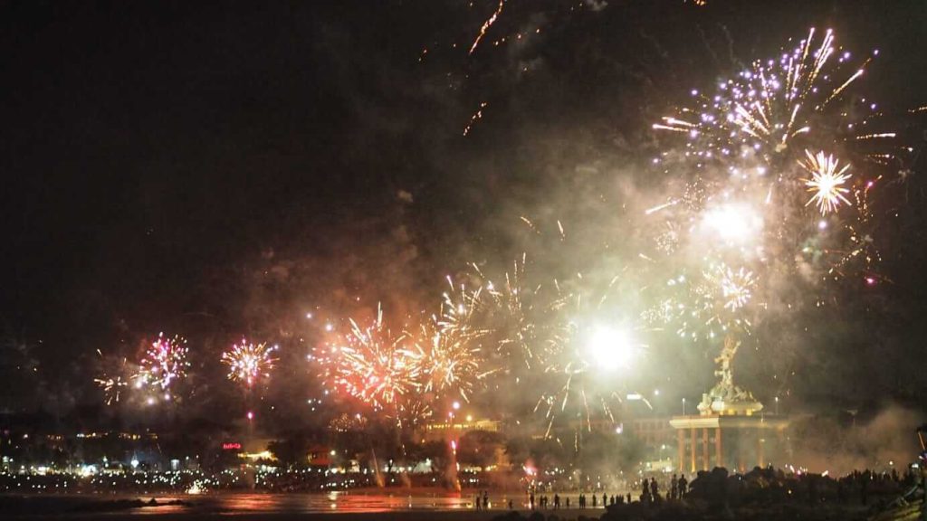 Kembang api menerangi langit Pantai Kuta dengan pantulan cahaya warna-warni di permukaan laut pada malam hari.