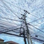 Garis-garis kabel yang bersilangan dengan latar langit, merefleksikan hubungan manusia dengan ruang dan teknologi.