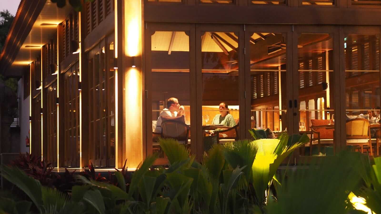 Orang-orang duduk berhadapan di dalam restoran dan lobi hotel, berbincang dalam suasana tenang.