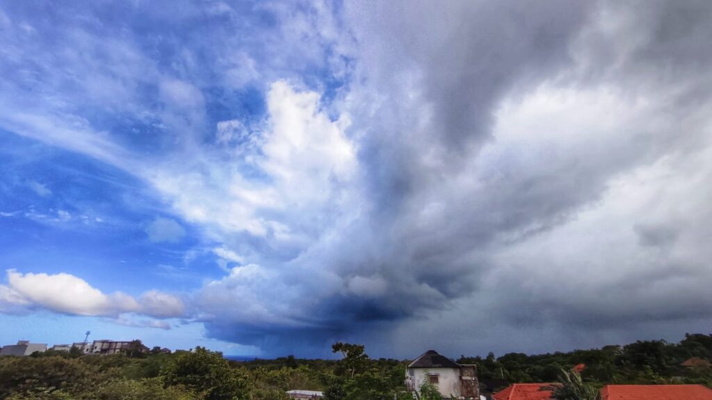 Langit memperlihatkan kontras antara biru cerah dan awan gelap yang menggantung tebal.