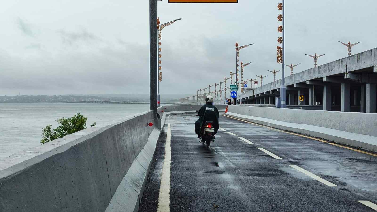 Pengendara melintas di Jalan Tol Bali Mandara saat hujan deras dengan mengenakan jas hujan.