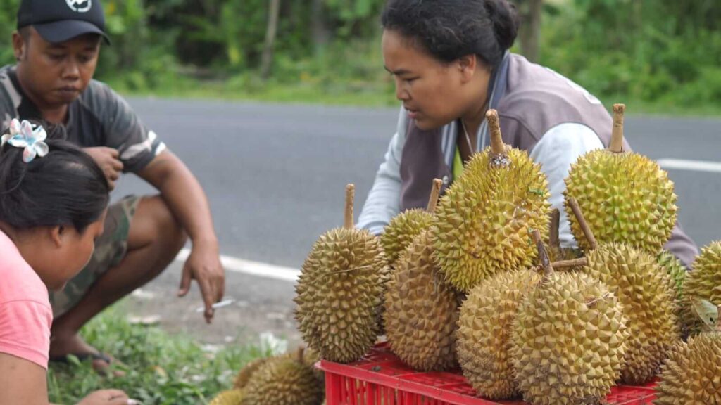 Seorang wanita bernama Putu mencicipi durian yang dijual di pinggir jalan.