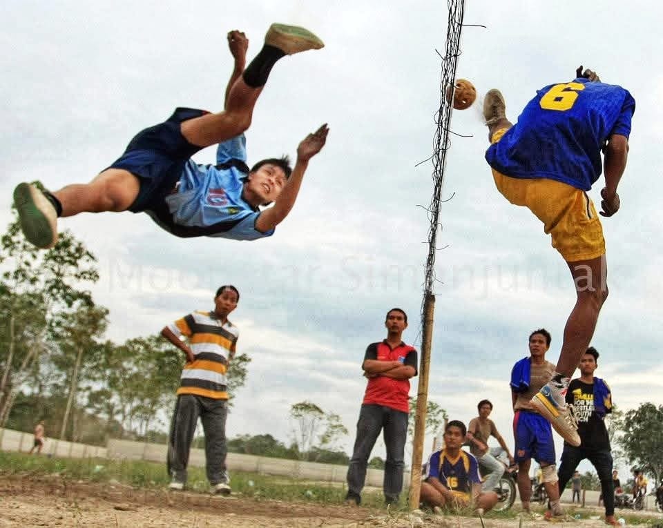 Pemain takraw melakukan aksi menendang bola melewati net dalam sebuah pertandingan.