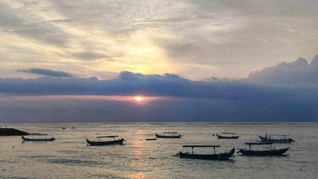 Panorama matahari terbenam di pantai dengan gradasi warna hangat.