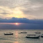 Panorama matahari terbenam di pantai dengan gradasi warna hangat.