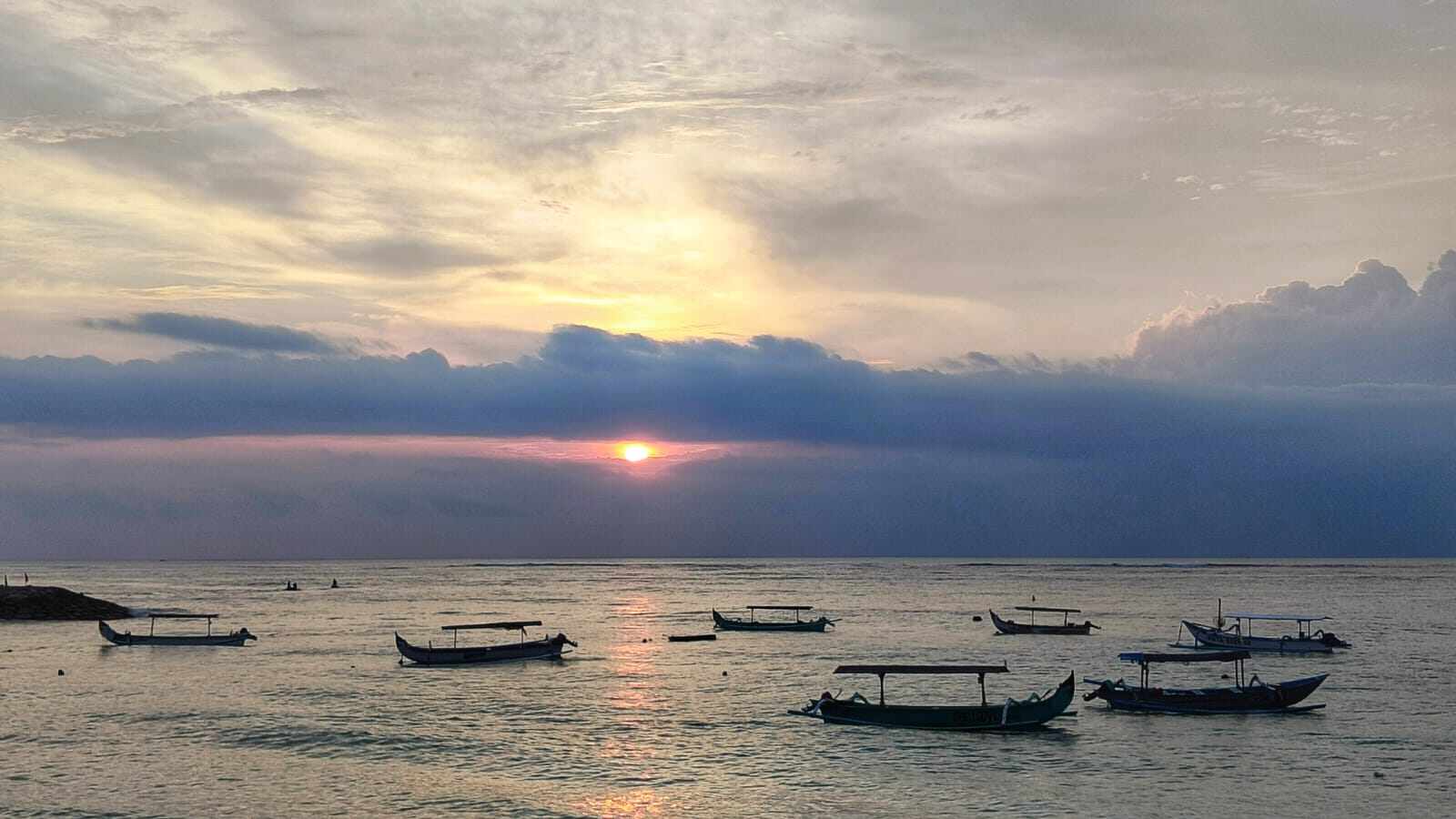 Panorama matahari terbenam di pantai dengan gradasi warna hangat.