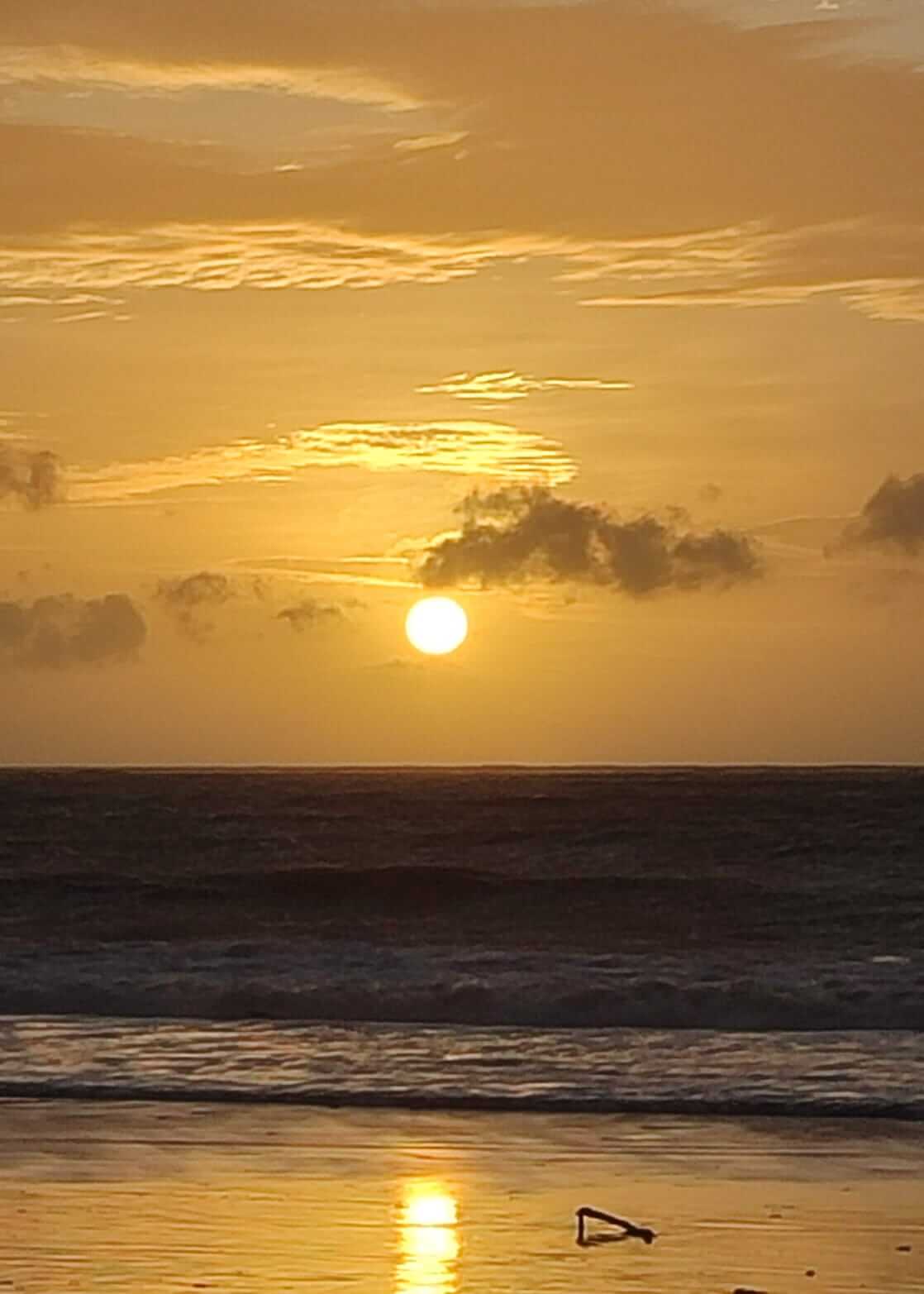 Suasana matahari terbenam di Pantai Jimbaran dengan langit berwarna hangat.