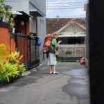 Seorang turis berdiri di gang kecil, memperhatikan vila potensial untuk menginap.