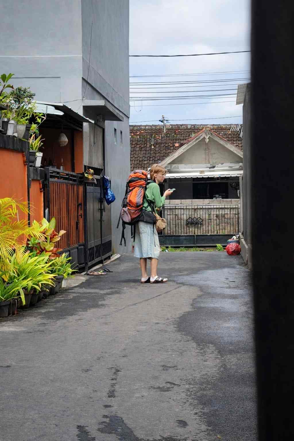 Seorang turis berdiri di gang kecil, memperhatikan vila potensial untuk menginap.