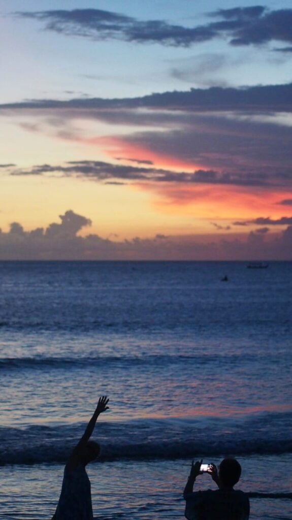 Suasana senja di Pantai Kuta dengan orang-orang menikmati pemandangan.