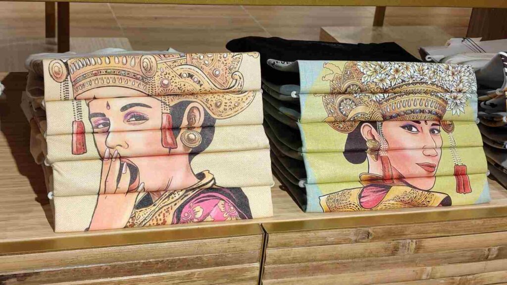 Kaos cendera mata bergambar ilustrasi perempuan Bali dengan busana adat dan ornamen tradisional.