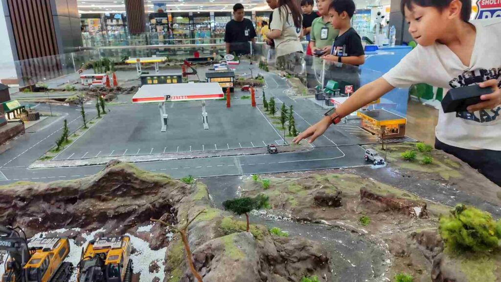 Anak-anak bermain mobil remote mini di arena khusus dengan miniatur jalan dan lanskap