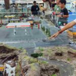 Anak-anak bermain mobil remote mini di arena khusus dengan miniatur jalan dan lanskap