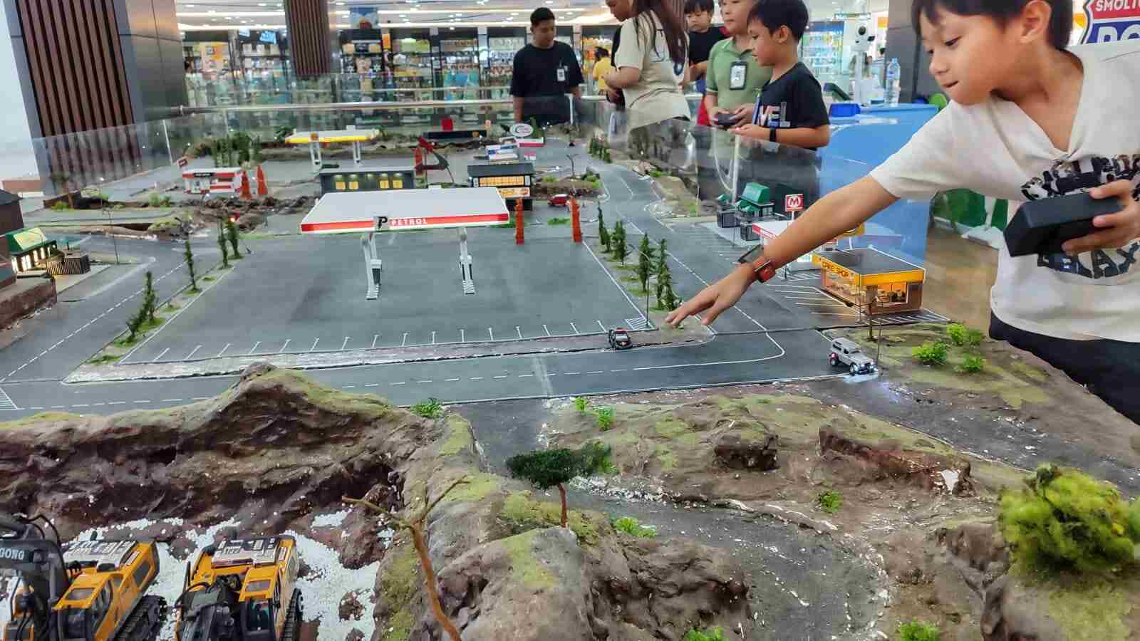 Anak-anak bermain mobil remote mini di arena khusus dengan miniatur jalan dan lanskap
