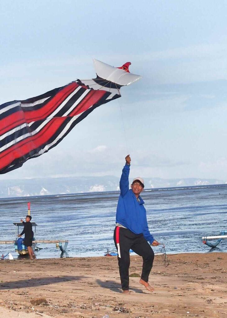 Layangan terbang di langit dengan suasana kebersamaan di bawahnya.