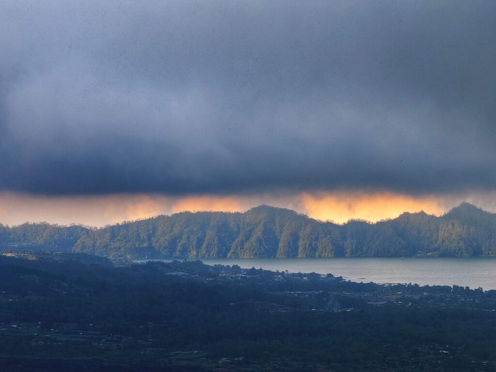 Cahaya jingga muncul di balik awan gelap menciptakan suasana langit yang dramatis