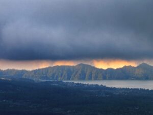 Cahaya jingga muncul di balik awan gelap menciptakan suasana langit yang dramatis