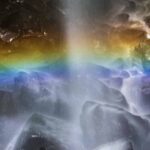 Pelangi muncul di antara gemuruh air yang mengalir, menciptakan pemandangan alam yang memikat