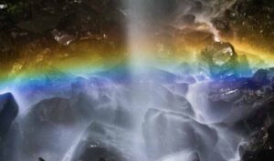 Pelangi muncul di antara gemuruh air yang mengalir, menciptakan pemandangan alam yang memikat