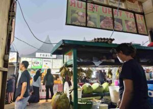 Deretan stan kuliner di sepanjang akses menuju area pertunjukan dengan pengunjung menikmati makanan dan minuman di kawasan acara.