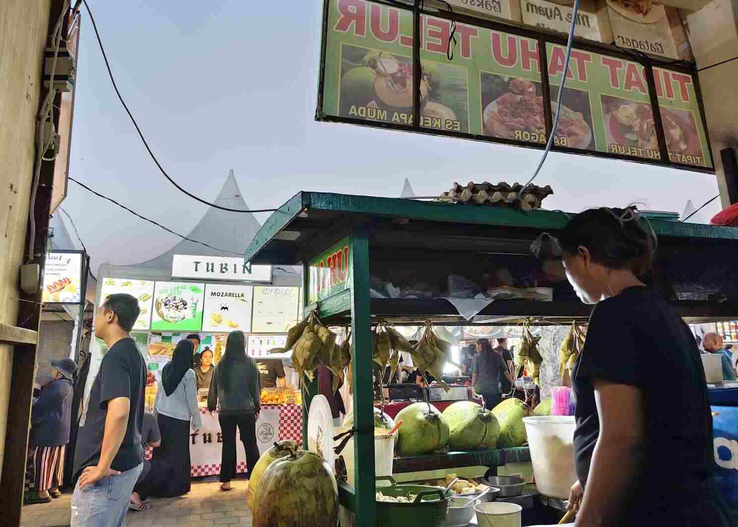 Deretan stan kuliner di sepanjang akses menuju area pertunjukan dengan pengunjung menikmati makanan dan minuman di kawasan acara.