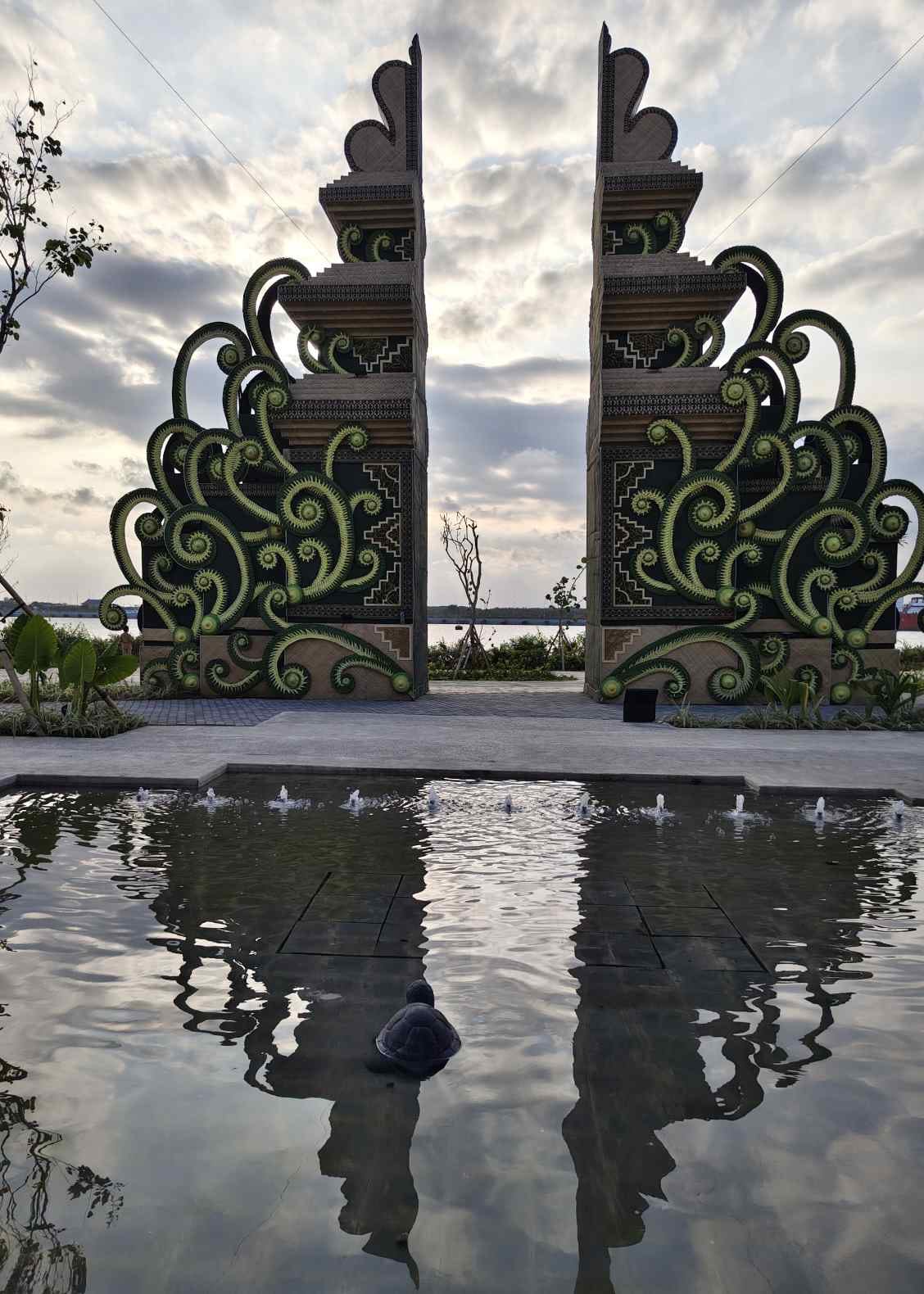 Arsitektur modern berpadu ornamen Bali dan lanskap tropis dengan pantulan air.