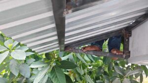 Pekerja konstruksi bekerja di celah sempit antara rangka besi dan lembaran metal di ketinggian.