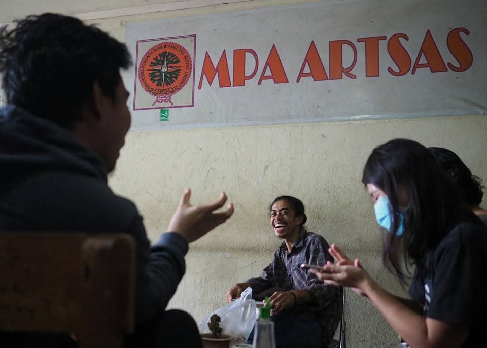 Mahasiswa duduk santai sambil bercengkerama dan tertawa bersama.