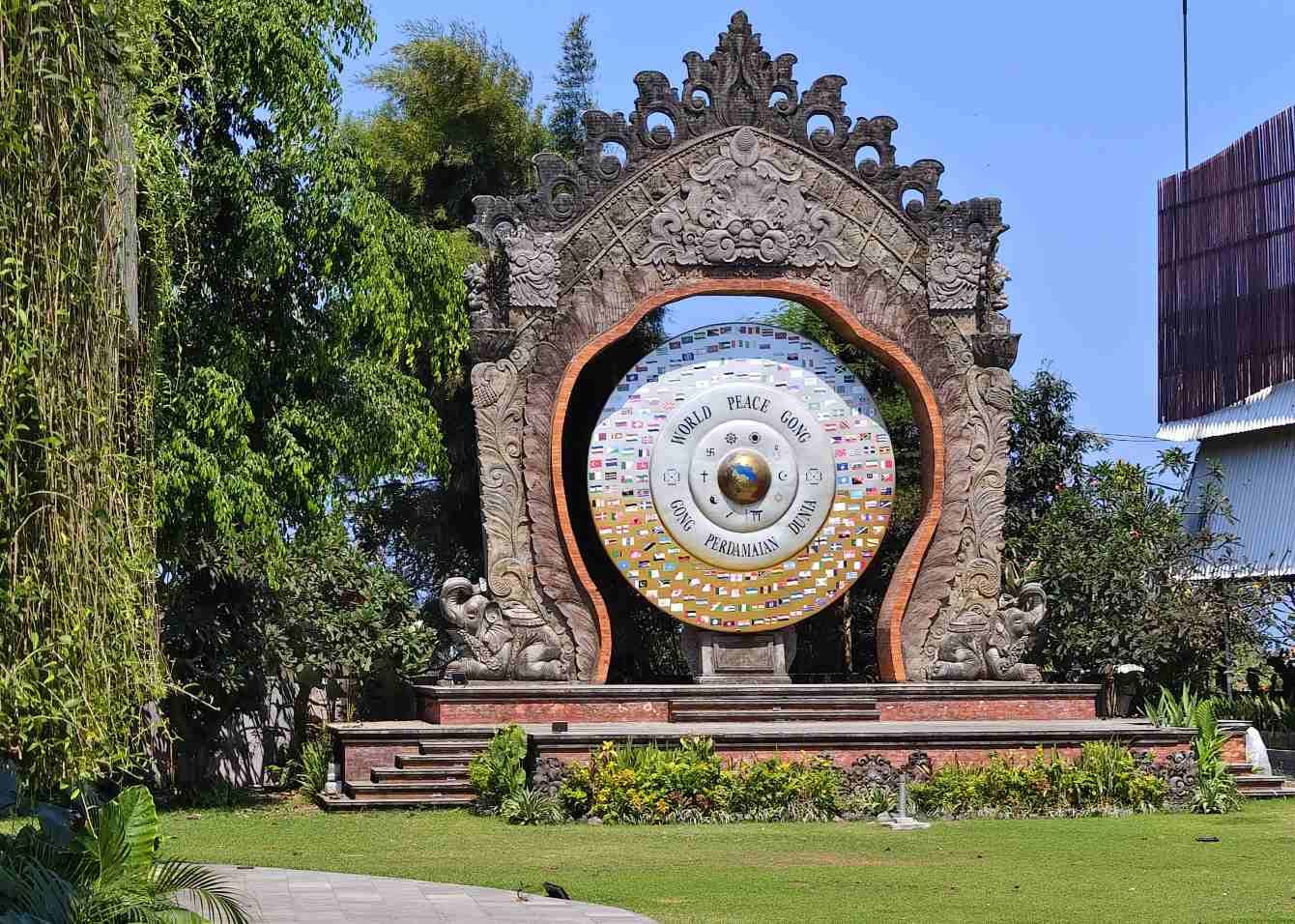 Gong Perdamaian Dunia dengan patung tokoh dunia, deretan bendera negara, dan simbol keberagaman agama.