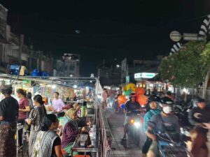 Suasana pasar malam yang ramai dengan pedagang kuliner, pakaian, minuman, dan aksesori.